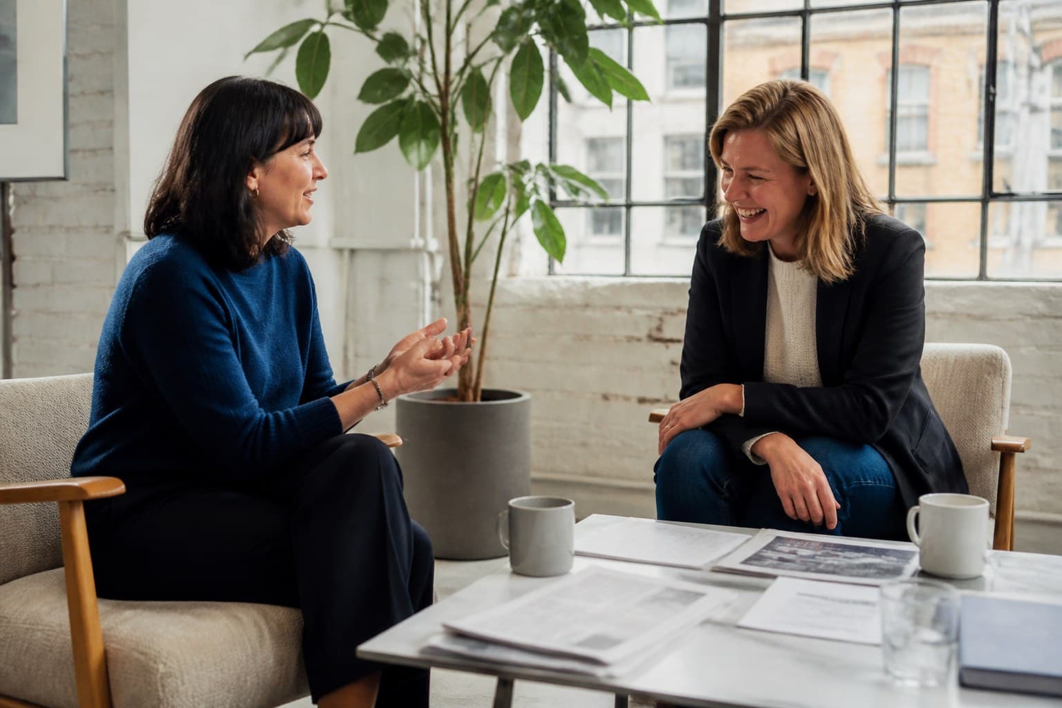 Two women talking over papers and coffee in a bright studio